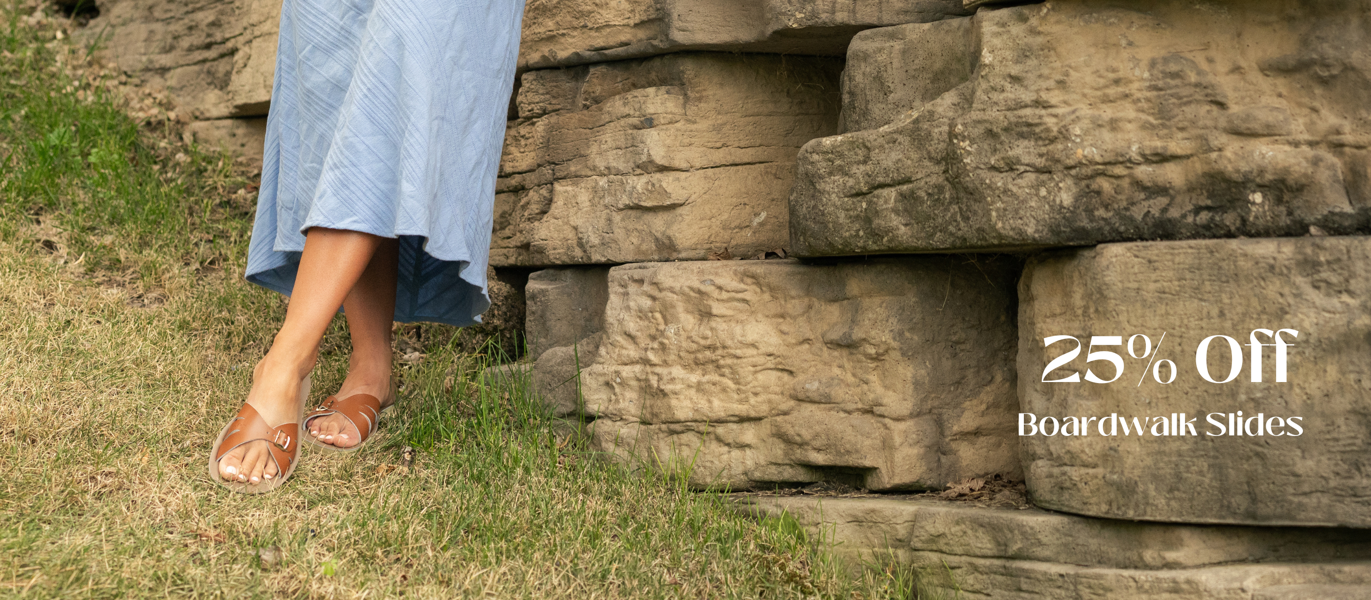 Person wearing sandals standing near a stone wall with promotional text for Boardwalk Slides.